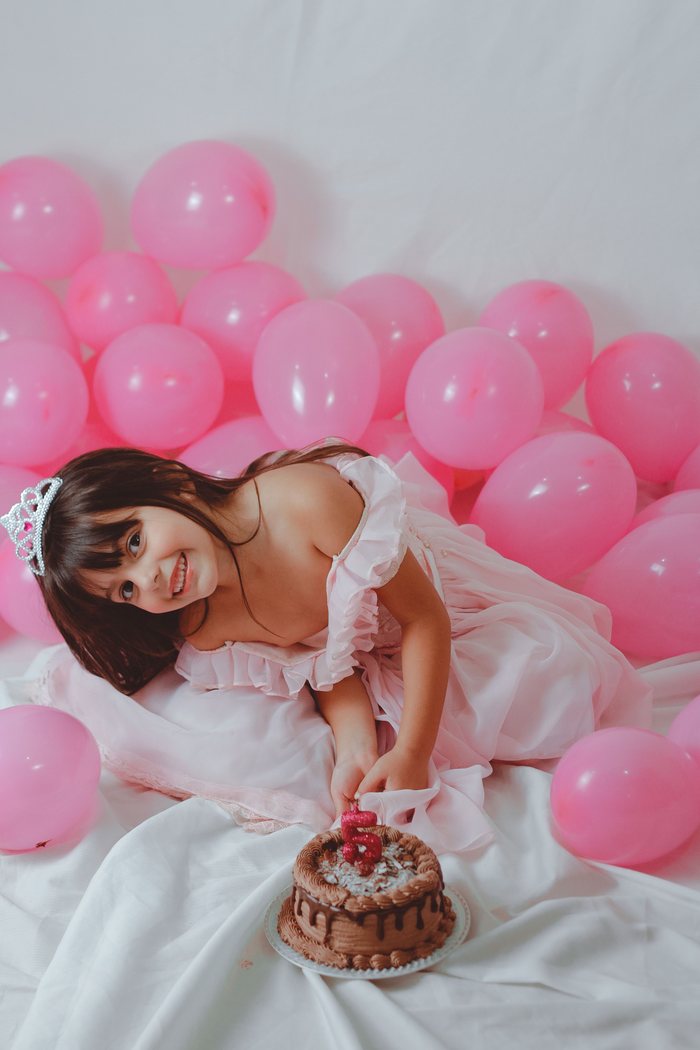 Girl in a pink dress with balloons and a fifth birthday cake