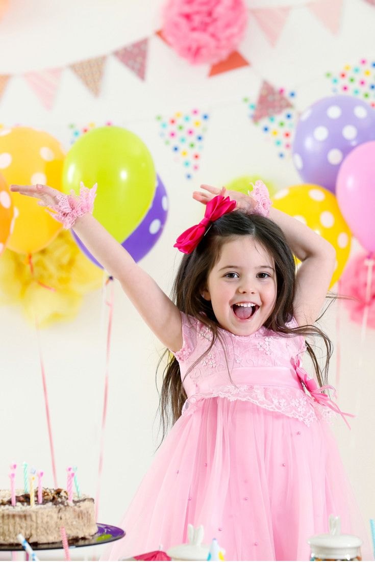 Happy girl in a pink party dress celebrating with balloons